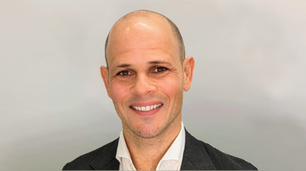 Professional headshot of a smiling bald man in a suit against a neutral background